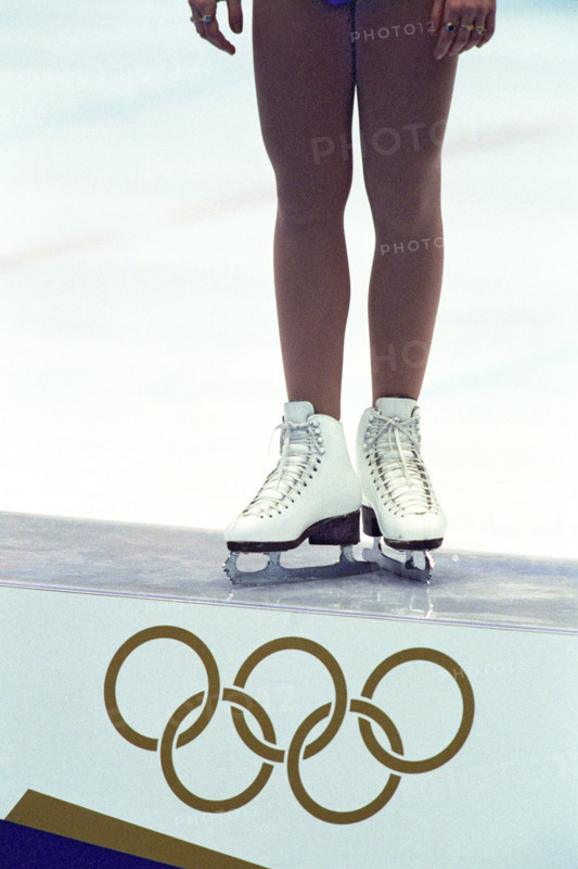 Detail of female figure skater standing atop the podium with the Olympic Rings.