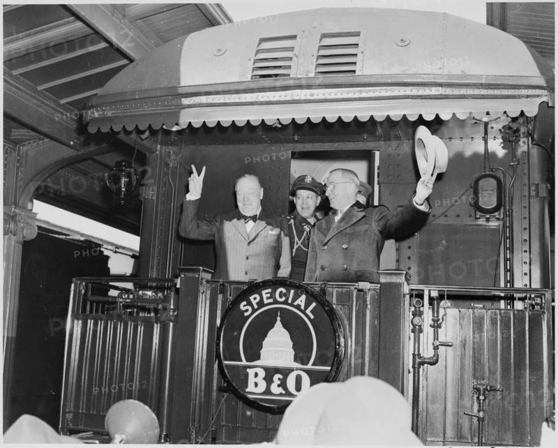 Photograph of President Truman waving his hat and Winston Churchill flashing his famous V for Victory sign from the rear platform of a special Baltimore & Ohio train (evidently en route to Fulton, Missouri for Churchill's Iron Curtain speech), as the President's Military Aide, General Harry Vaughan, looks on.