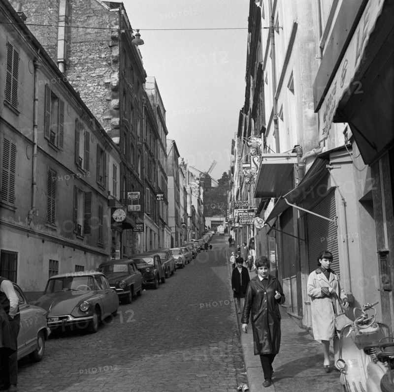 Pariser Bilder [The street life of Paris]  Rue Lepic in Montmartre, with Le Moulin de la Galette at the end of the street Annotation: Le Moulin de la Galette was a popular dance venue and figures on paintings by Vincent van Gogh, Henri Toulouse-Lautrec, Pablo Picasso and Auguste Renoir Date: 1965 Location: France, Paris Keywords: windmills, street images