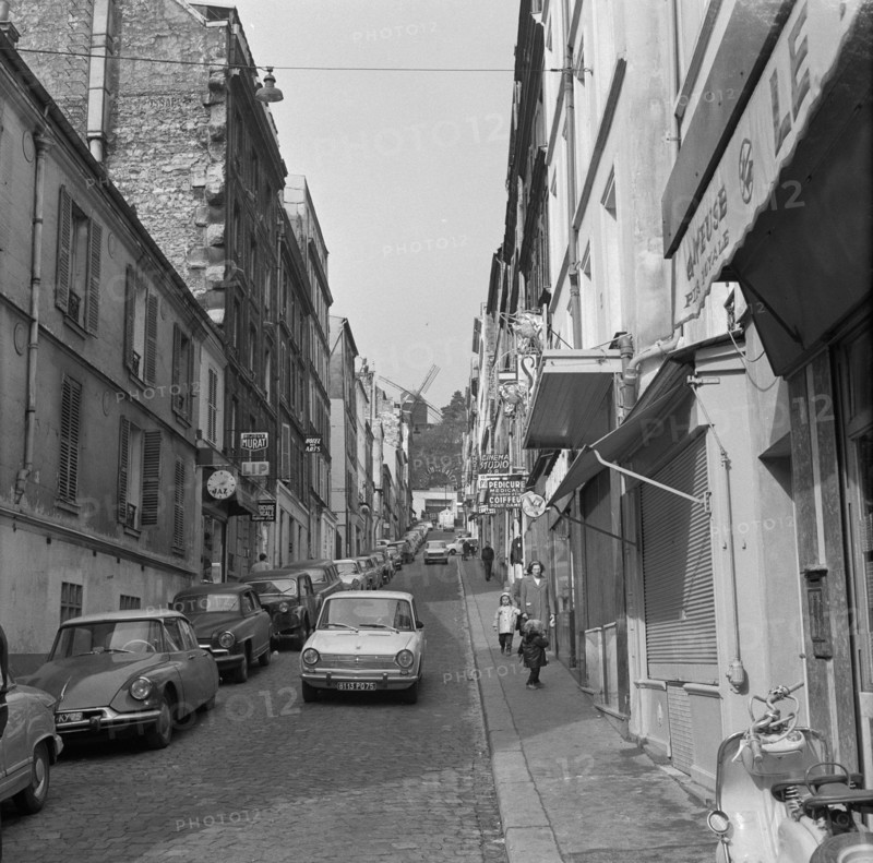 Pariser Bilder [The street life of Paris]  Rue Lepic in Montmartre, with Le Moulin de la Galette at the end of the street Annotation: Le Moulin de la Galette was a popular dance venue and figures on paintings by Vincent van Gogh, Henri Toulouse-Lautrec, Pablo Picasso and Auguste Renoir Date: 1965 Location: France, Paris Keywords: windmills, street images