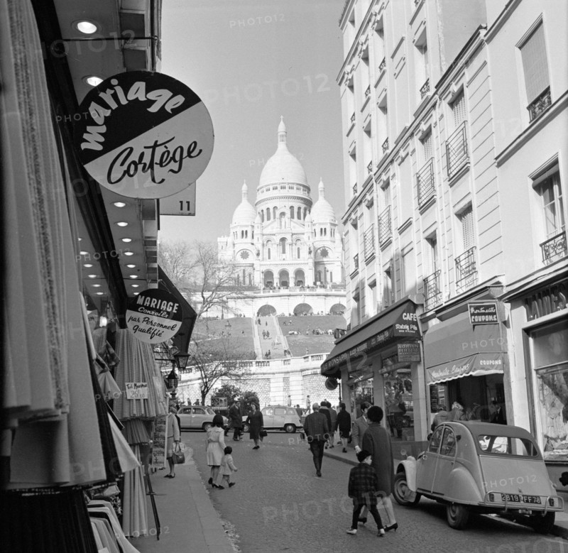 Pariser Bilder [The street life of Paris]  Shopping street with a view of the Basilique du Sacré-Coeur Annotation: The Basilique du Sacré-Coeur (1875-1914) was built on the occasion of the deaths that fell during the Franco-German War of 1870-1871, the design was by architect Paul Abadie Date: 1965 Location: France, Paris Keywords: basilicas, churches, street sculptures, shops Personal name: sacre coeur Institutional name: Sacré Coeur