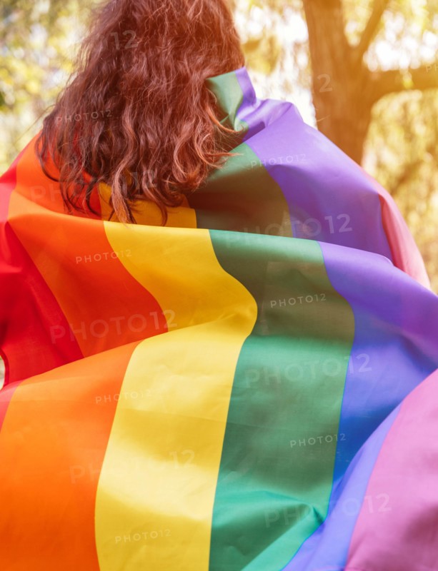 Lesbian woman wearing an LGBTQ flag, symbol for the homosexual community, as a cape. Gay rainbow colors flag for pride month and the celebration day o