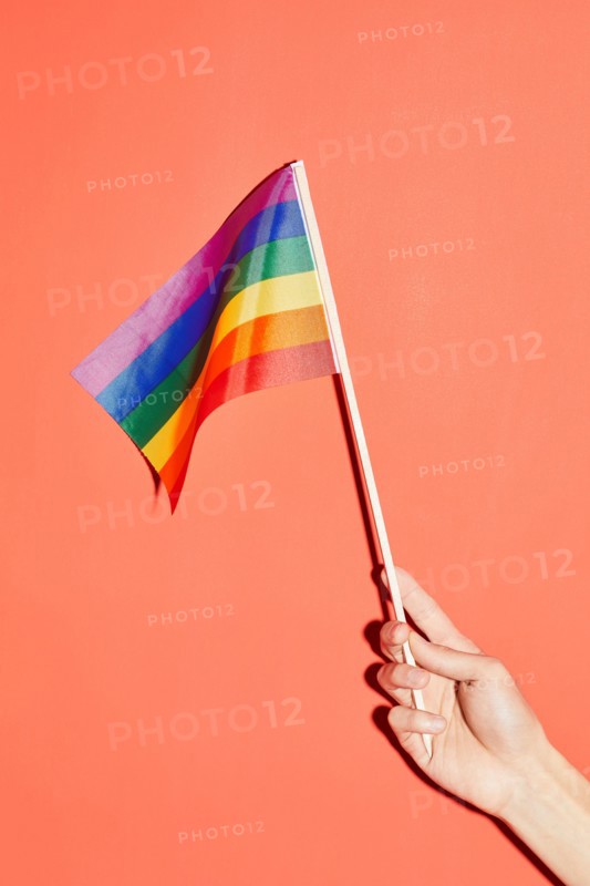 Vibrant shot of female hand holding rainbow flag at pink background as symbol for pride month LGBTQ