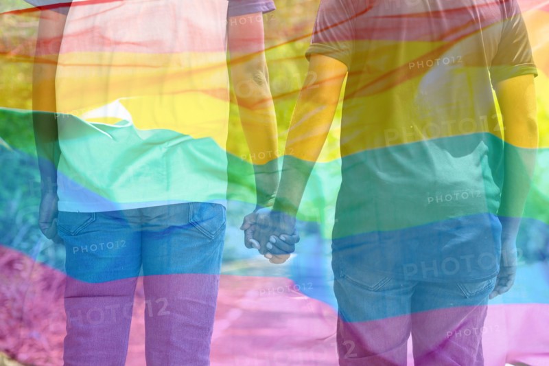 Double exposure shot of flying lgbtq flag with couple joining hands in background - concept of pride month celebration, freedom and quality