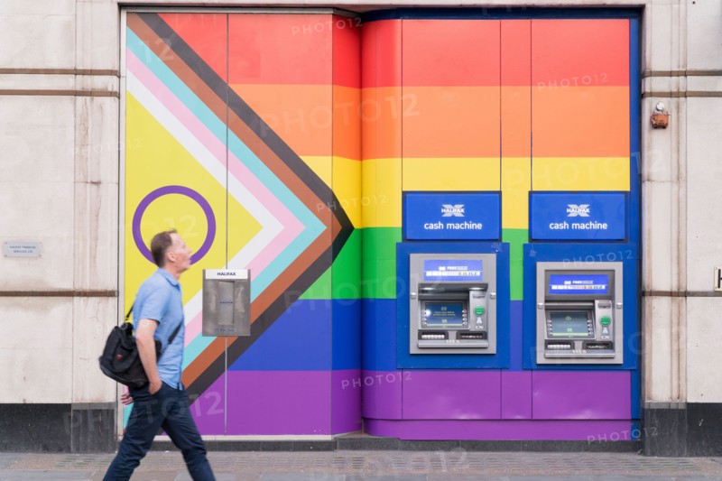 A man walks past two cash machines on the wall painted with rainbow colours during celebration of Pride Month England UK