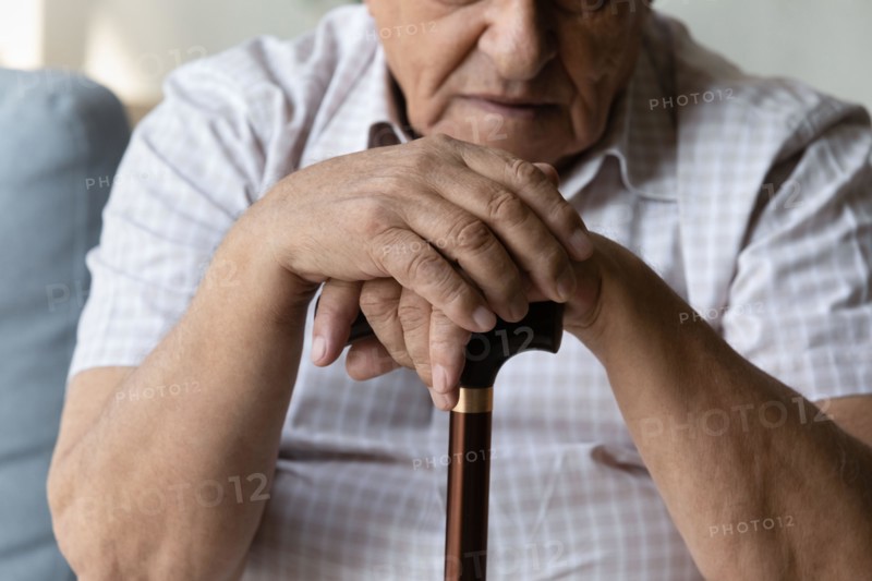 Closeup cropped old man holding hands on walking cane.