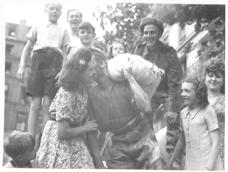 A British soldier unloads flour in the Les Halles market in Paris while pausing to interact with a young French girl, part of post-liberation food supplies.