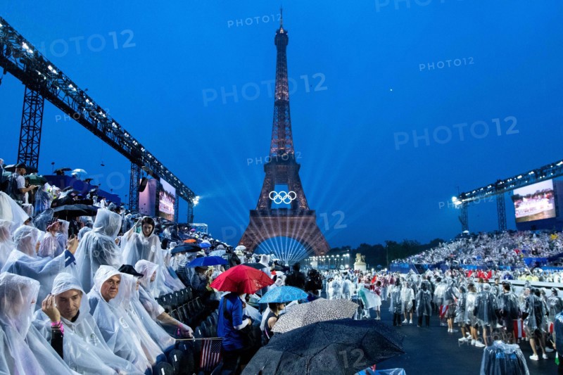 Symbolbild / Themenfoto Eiffelturm mit Beleuchtung und olympischen Ringen, davor Zuschauer am Trocadero im Regen mit Schirm und Regenponcho im Regen, FRA, Olympische Spiele Paris 2024, Eroeffnungsfeier, Opening Ceremony, 26.07.2024  Foto: Eibner-Pressefoto/Roger Buerke
