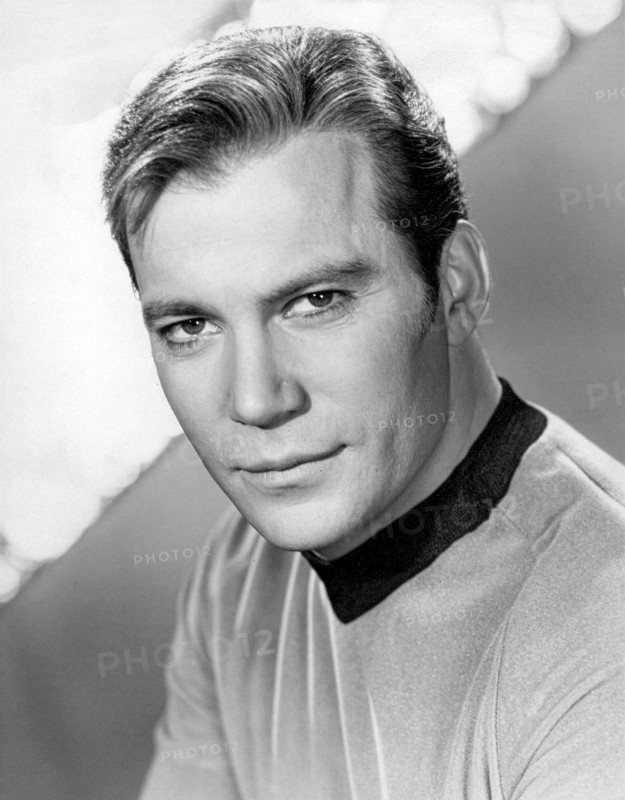 This 1960s black and white publicity still features William Shatner as Captain James T. Kirk from the original Star Trek television series. He is depicted in his iconic gold Starfleet uniform, looking directly at the camera with a confident expression. The image captures the essence of the beloved science fiction character during the show's initial run.