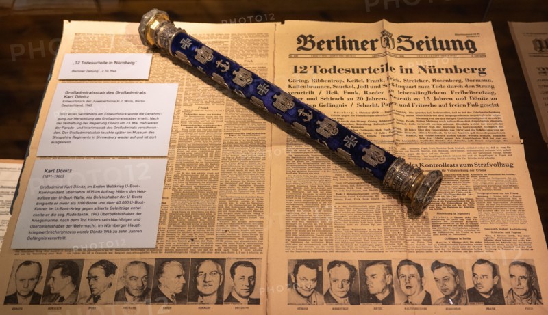 Hamburg, Germany - 7 Apr 25: Museum display featuring a Berliner Zeitung page about Nuremberg trial verdicts alongside a decorated admiral baton, Inte