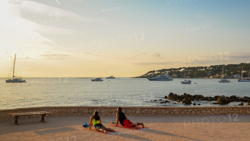 A man and a woman practice yoga early in the morning overlooking Antibes, Cote d'Azur, France