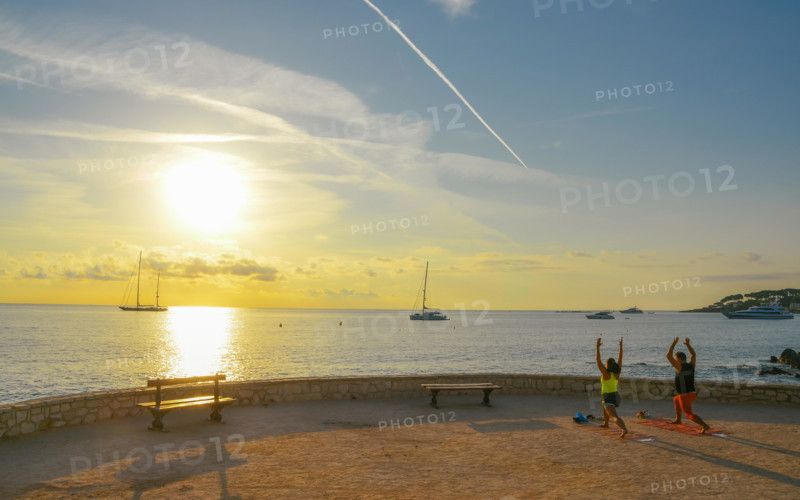 A man and a woman practice yoga early in the morning overlooking Antibes, Cote d'Azur, France