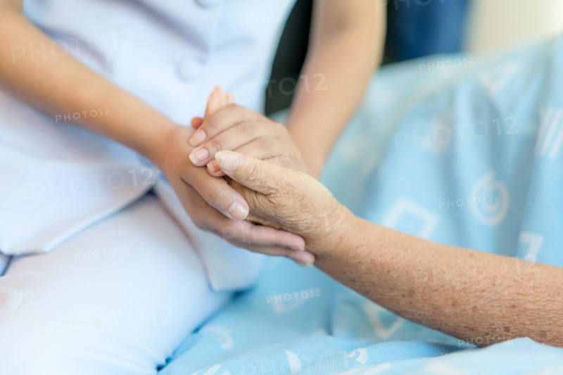 Nurse sitting on a hospital bed next to an older woman helping hands, care for the elderly concept