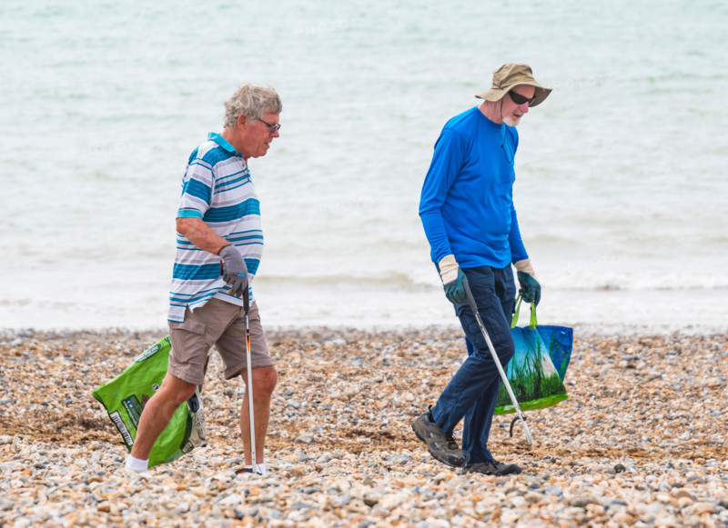 Pair of good samaritan volunteer men picking up litter from a beach in the UK.