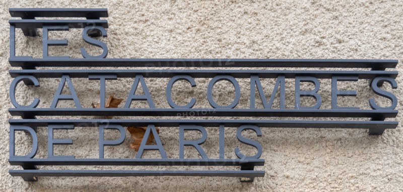 Paris, France - 8 Nov 24: Close-up of metal lettering reading "Les Catacombes de Paris" mounted on a stone facade in Paris, Île-de-France, France.