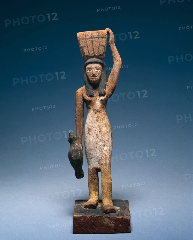 Female Offering Bearer, 2000-1801 BC. Egypt, Middle Kingdom, late Dynasty 11 to early Dynasty 12. Painted wood, figure of tamarisk (?), base of sycamore fig; overall: 25.8 x 7.9 x 12.2 cm (10 3/16 x 3 1/8 x 4 13/16 in.).
