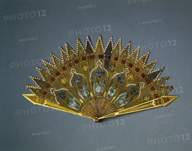 Brise Fan:  Gothic Revival Style, c. 1830. England (probably), 19th century. Gilt metal, enamel, horn, pigment, spangles, ribbon; radius: 18.8 cm (7 3/8 in.); spread: 35 cm (13 3/4 in.).
