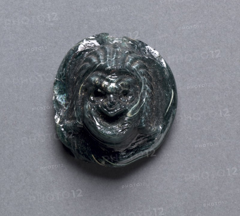 Comic Mask, c. 1st Century AD. Greece, Greco-Roman Period, late Ptolemaic Dynasty to Roman Empire. Dark green glass; diameter: 3.6 cm (1 7/16 in.); overall: 1.7 cm (11/16 in.).