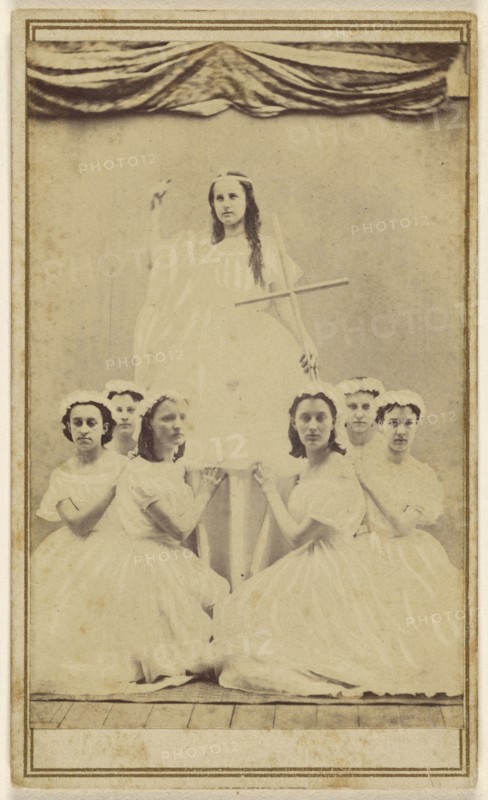 Female group portrait, six in white gowns kneeling, one standing holding a cross; about 1865; Albumen silver print