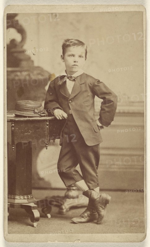 Young boy in suit standing and posed near a table with a hat on top; McClain, American, active 1880s, about 1865; Albumen