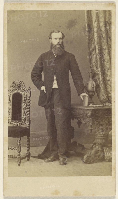 Full-bearded man, standing, with hand on book resting on table; Schwarzschild & Co; 1860s; Albumen silver print