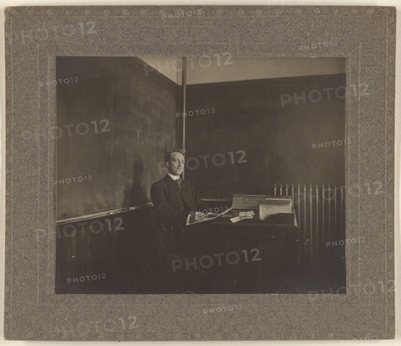 Portrait of a male teacher seated at his classroom desk; American; about 1900; Gelatin silver print