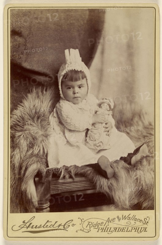 Baby girl in bonnet, seated, holding a doll; A. Husted & Company; about 1880; Albumen silver print