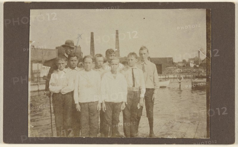 Eight young men standing on a dock near a river, with a man wearing a hat; 1875 - 1885; Albumen silver print