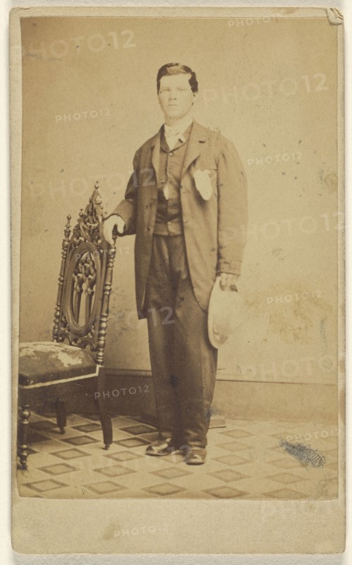 man standing holding his hat in one hand and holding a chair back with the other; Lew Horning, American, active Philadelphia