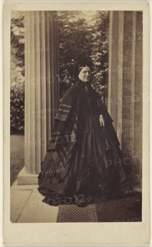 elderly woman standing outside near column at house entrance; J.G. & E.G. Short, British, 1865 - 1875; Albumen silver print