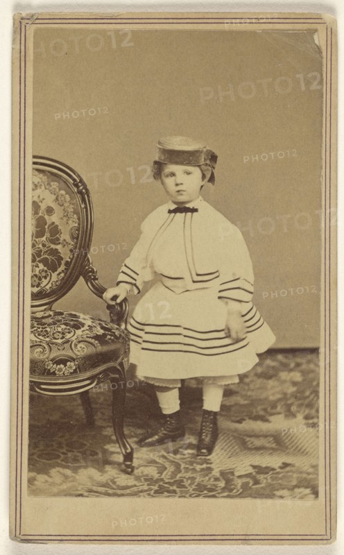 little girl wearing a pill-box hat, standing, holding the arm of a chair; Churchill & Denison; 1865 - 1875; Albumen silver print