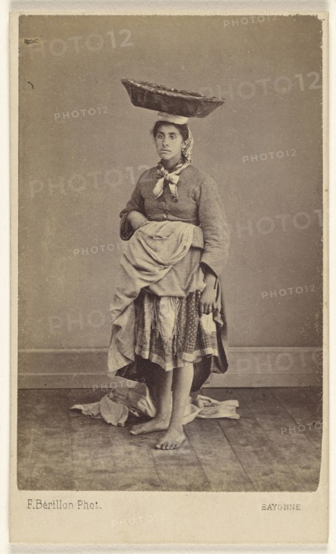 woman of Bayonne, France, wearing her native costume, standing, with a basket on top of her head; Ferdinand Berillon French