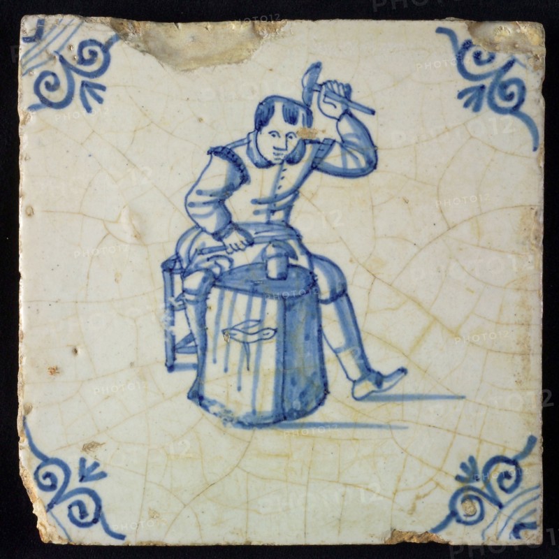 Occupation tile, blue with seated blacksmith with raised hammer and anvil, corner motif oxen head, wall tile tile sculpture