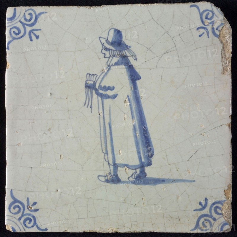 Occupation tile, blue with standing nobleman with handkerchief In his hand, long cloak, top hat, corner pattern ox head, wall