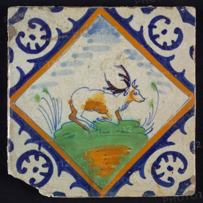 Animal tile, kneeling deer on small ground within square with palm corner in green, yellow, brown and blue on white, wall tile