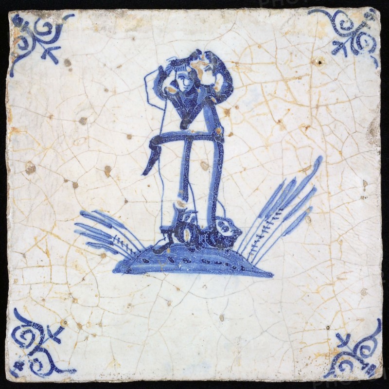 Figure tile, blue with man (sailor?) With arms up on ground with fish At his feet, corner pattern ox head, wall tile