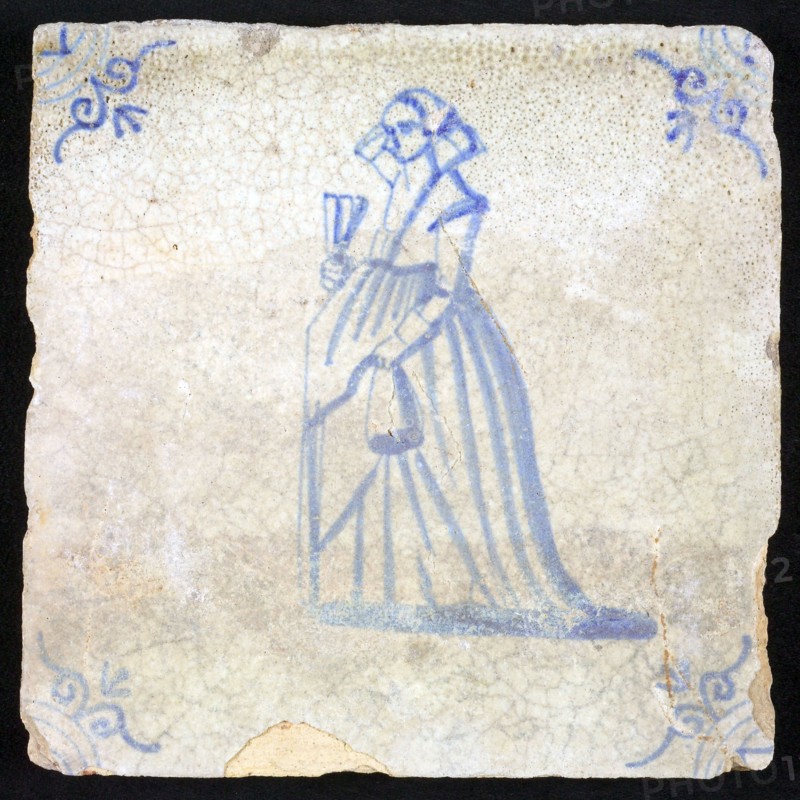 Figure tile, blue with lady with fan, lifts her skirt with hand, corner motif of ox's head, wall tile tile sculpture ceramic