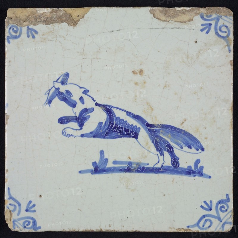 Animal tile, jumping fox to the left with fish in its mouth, in blue on white, corner motif of ox's head, wall tile
