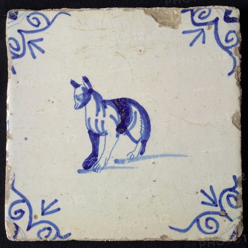Animal tile, standing dog to the left with strange legs, in blue on white, corner motif ox's head, wall tile tile sculpture