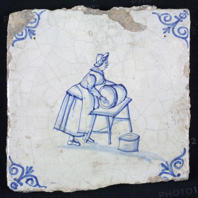 Figure tile, blue with woman cleaning barrel, on table, corner motif oxen head, wall tile tile sculpture ceramic earthenware