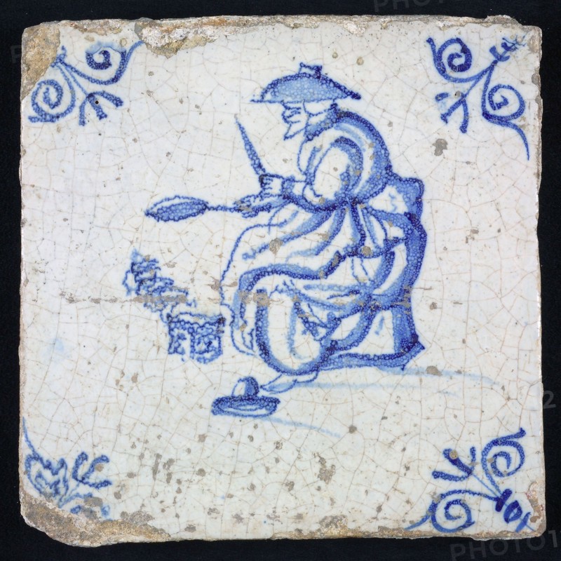 Tile, blue with woman sitting with frying pan in her hand, corner motif-shaped ox-head, wall tile tile sculpture ceramic