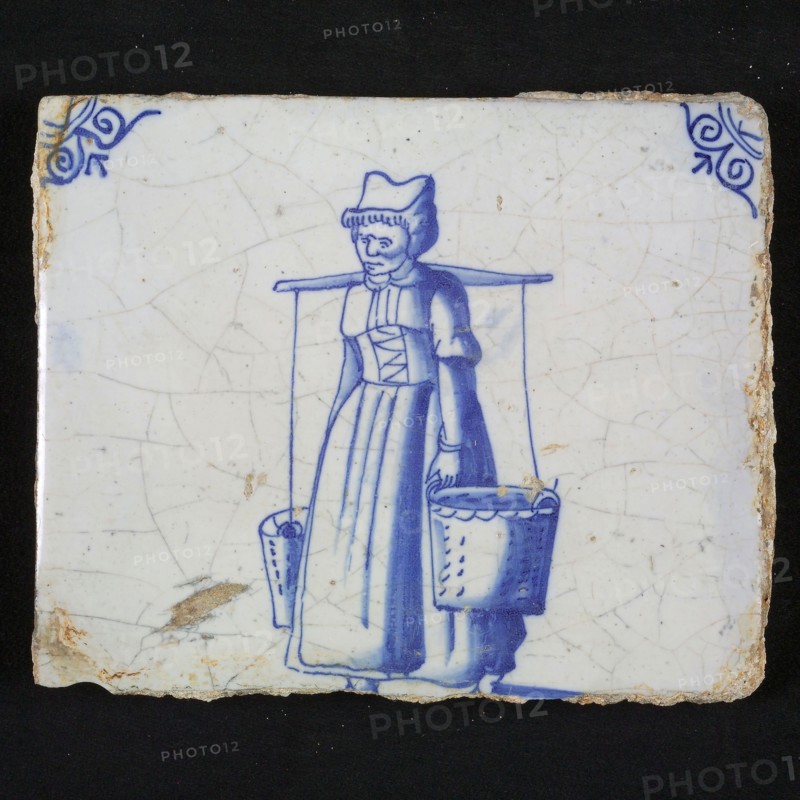 Figure tile, blue with peasant woman with yoke and two buckets, laced straitjacket, corner motif, ox-head, wall tile