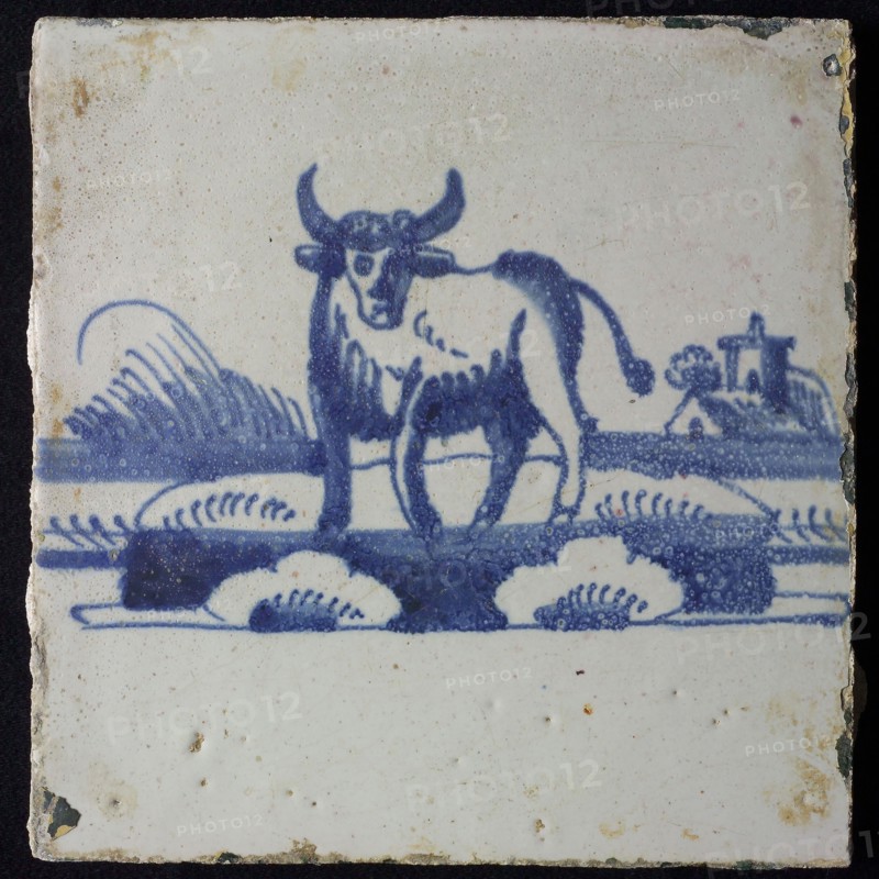 Animal tile, standing ox to the left on continuous plot, buildings with tower in the background, in blue on white, no corner