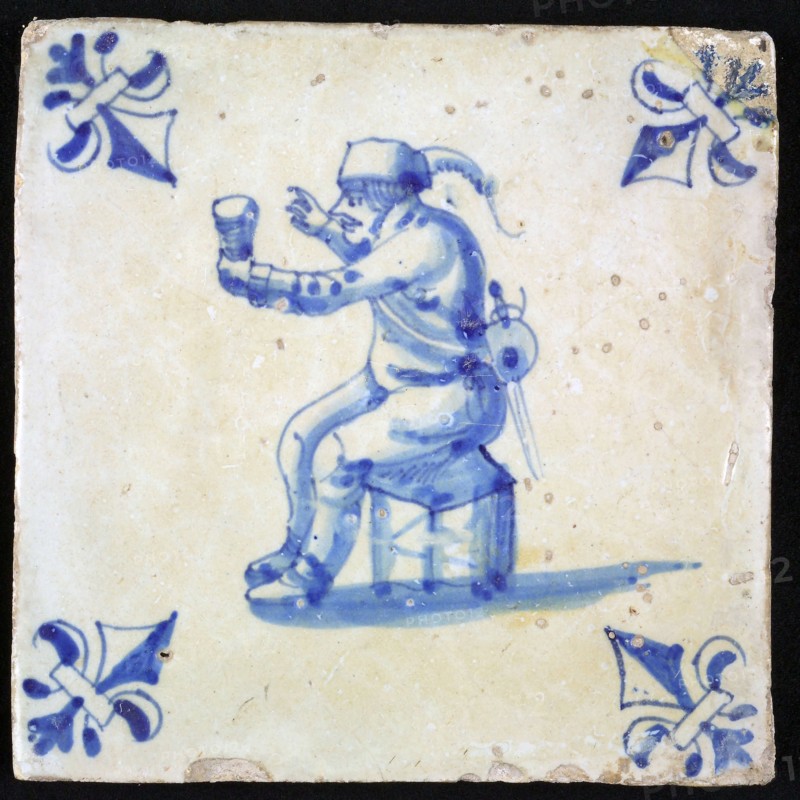 Figure tile, blue with man sitting on stool with cup in hand, corner pattern lily, wall tile tile sculpture ceramic earthenware
