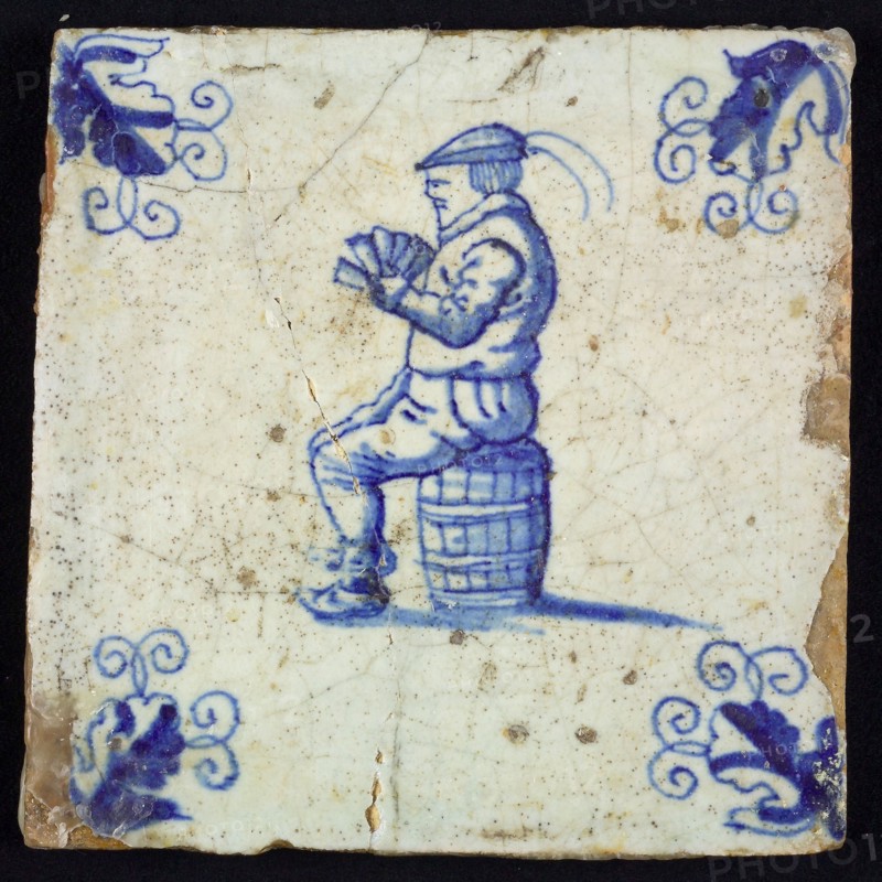 Figure tile, blue with man sitting on barrel with playing cards in hand, corner motif wader, wall tile tile sculpture ceramic