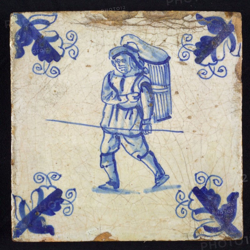 Figure tile, blue with walking man with basket or basket on the back and staff in the hand, corner motif, wall tile