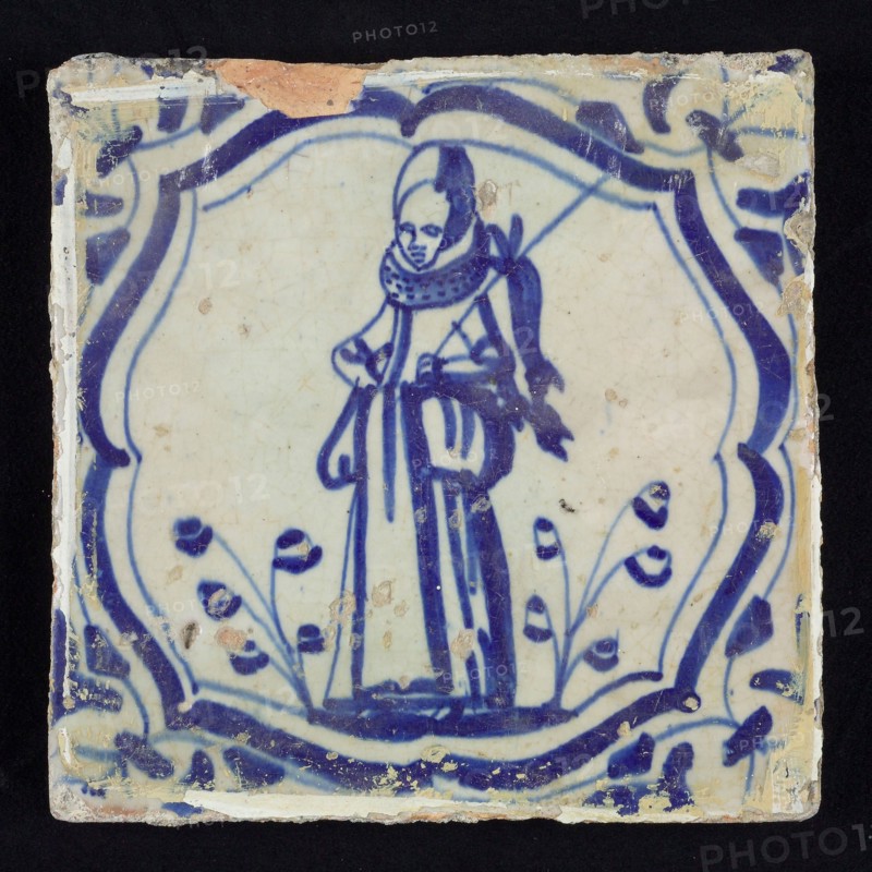 Figure tile, blue with hunting scene with woman with staff with dead rabbit, curly braces with corner motif, wall tile