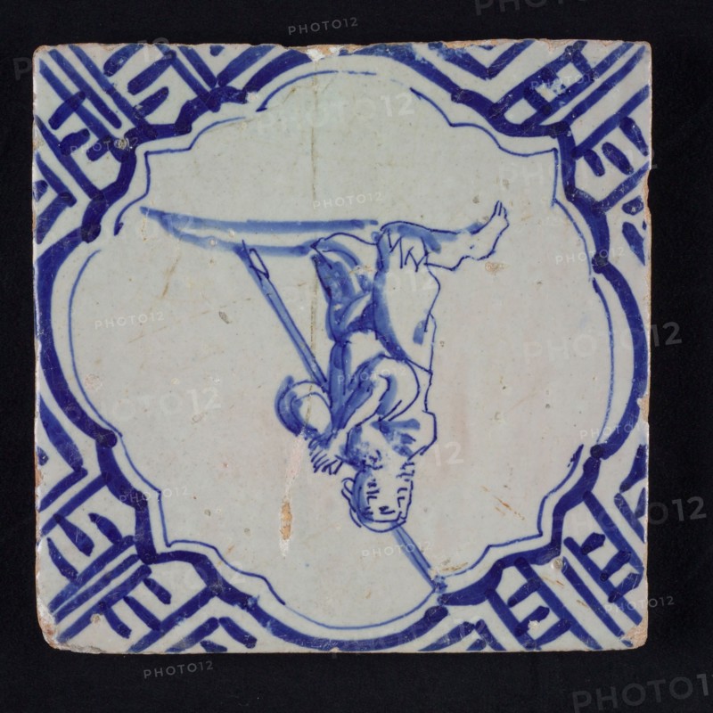 Figure tile, blue with man on the knees, pleading or praying, in scalloped frame with braces, corner motif meander, wall tile
