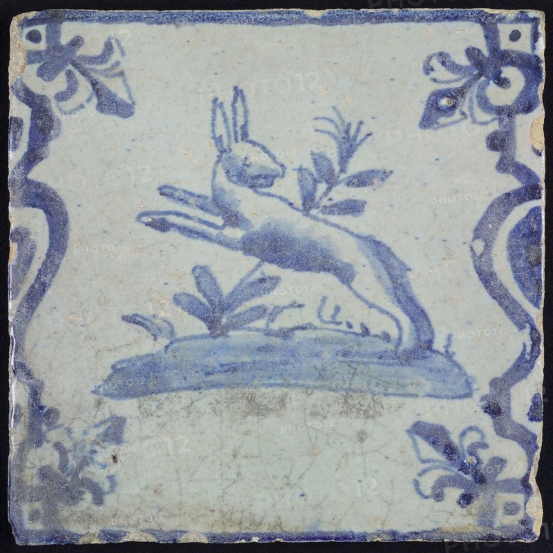 Animal tile, jumping hare to the left on plot between balusters, in blue on white, corner pattern French lily, wall tile