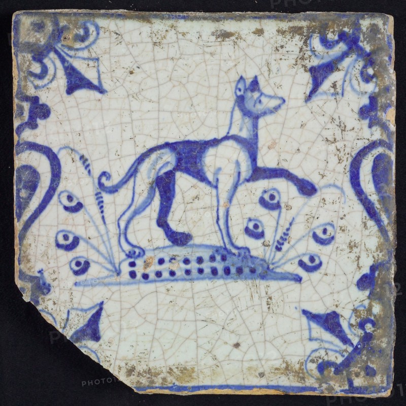 Animal tile, running dog to the right on plot between balusters, in blue on white, corner pattern French lily, wall tile